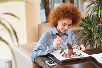 Cute curly young woman eating dessert in cafe