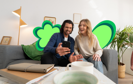 Une femme et un homme sont assis sur le canapé, regardant leur téléphone et semblent heureux.